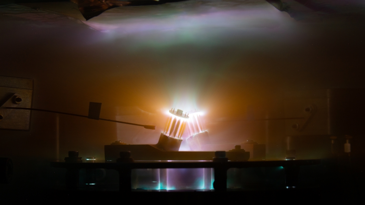 Brightly-coloured plasma is shown glowing outwards from two small tilted cylindrical arrays of thin carbon wires.